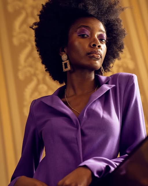 Portrait of a woman with an afro wearing a purple suit against a gold backdrop